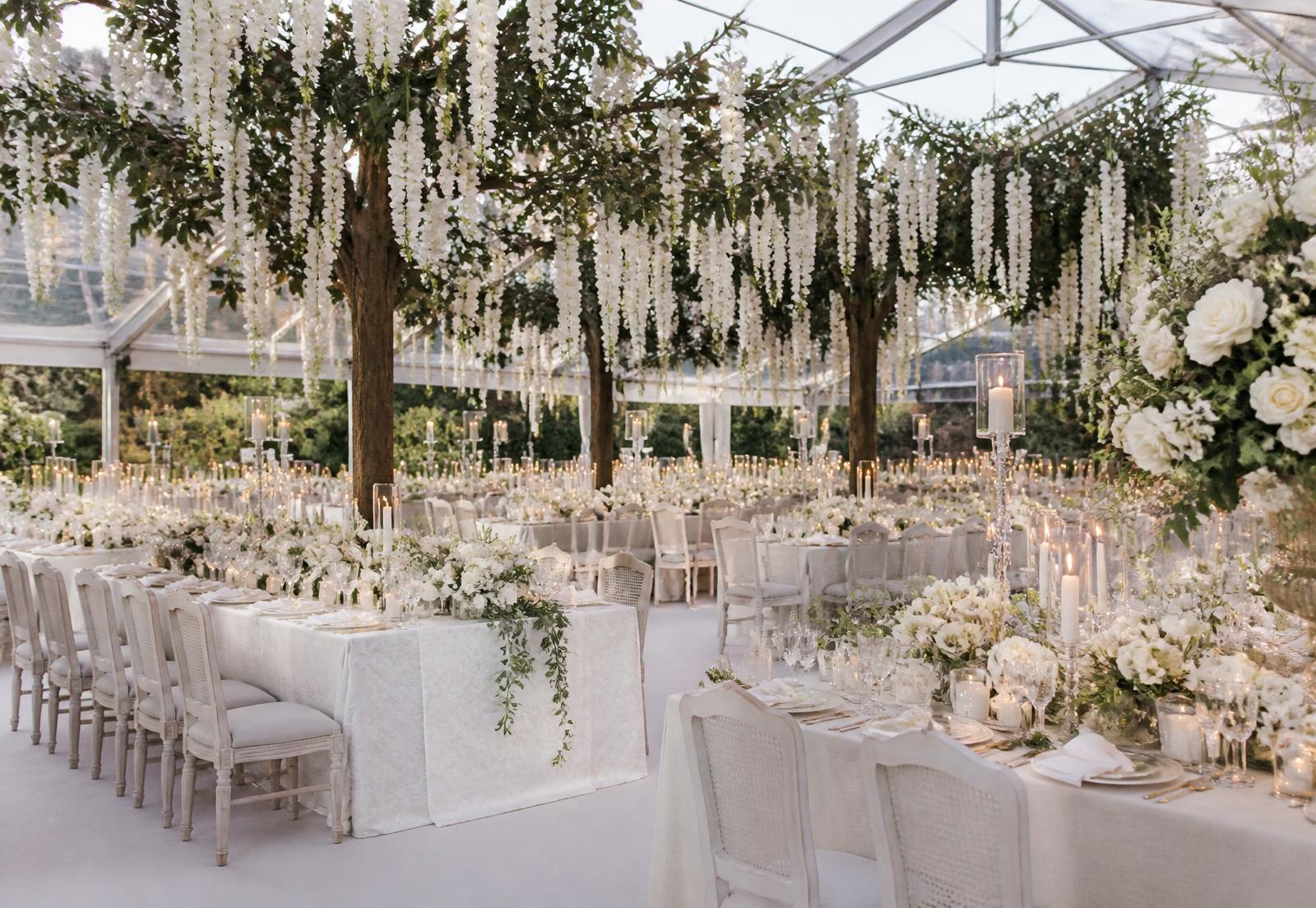 Luxury garden marquee reception with suspended white florals and candlelit tables